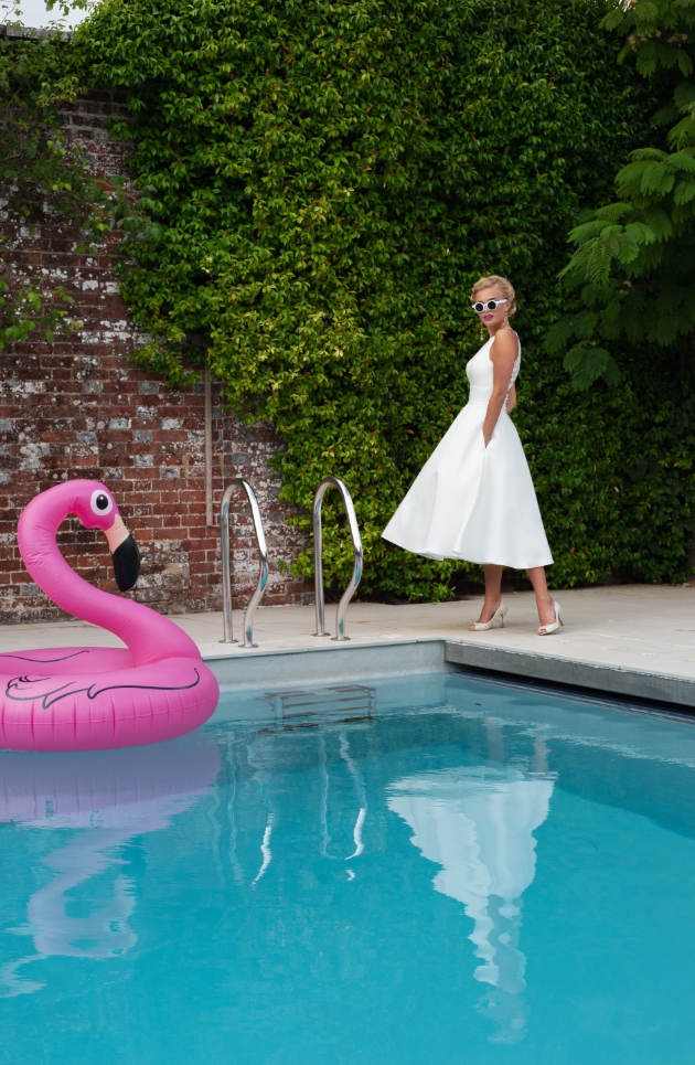 A full-skirted Mikado dress featuring a halter style neckline model is standing by the pool