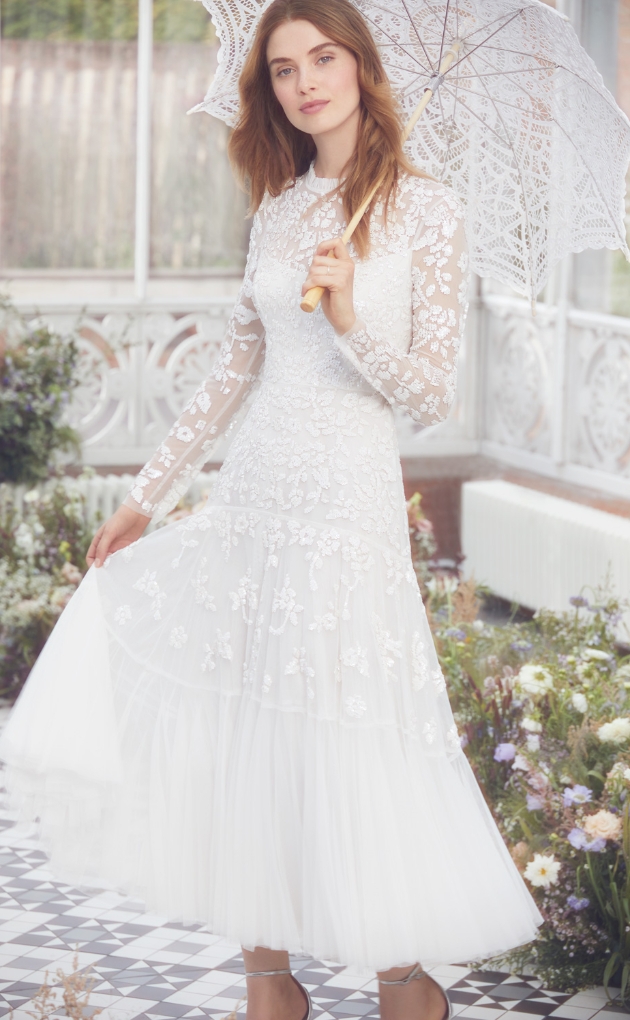 Model is in a summer house wearing a ivory lace gown decorated with sequins and petal embellishments 