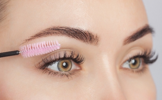 close up of woman applying mascara with a pink spoolie