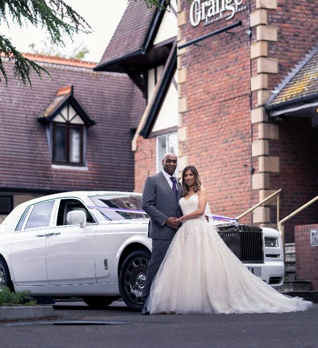 Couple pose with wedding car