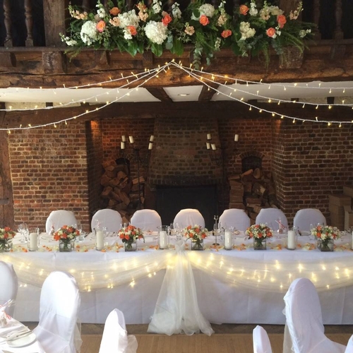 top table at a wedding reception covered in wedding flowers, with fairylights draped above and balcony flowers