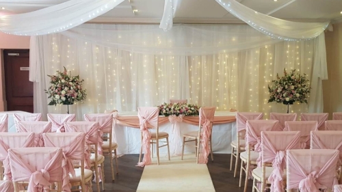 wedding ceremony room with chairs with pink sashes, an aisle and flowers the the registration desk
