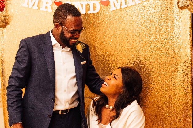 bride sitting down, groom standing with gold sequin backdrop