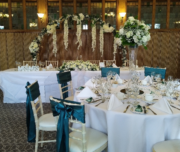 wedding reception room with top table and circle table with floral arch behind the top table and a flower display on round table