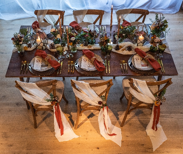 rustic table setting for six of wood, with runner and flowers and chairs with red sashes