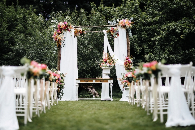 outdoor ceremony with arch and wooden white chairs creating aisle