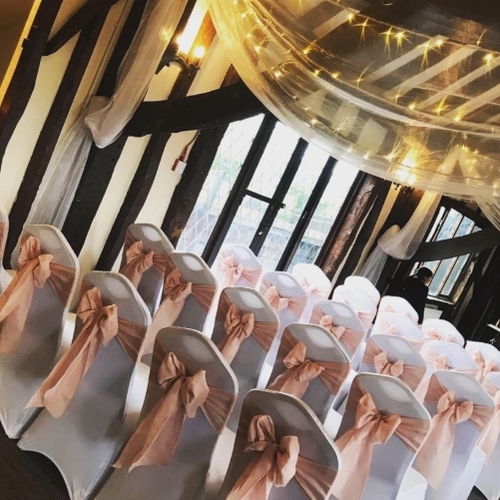 white chair covers on chairs with pink bows and a drape above of fairylights 