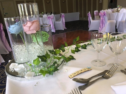 top table setting with scrabble tiles for the name and three cylinder vases of water and flowers