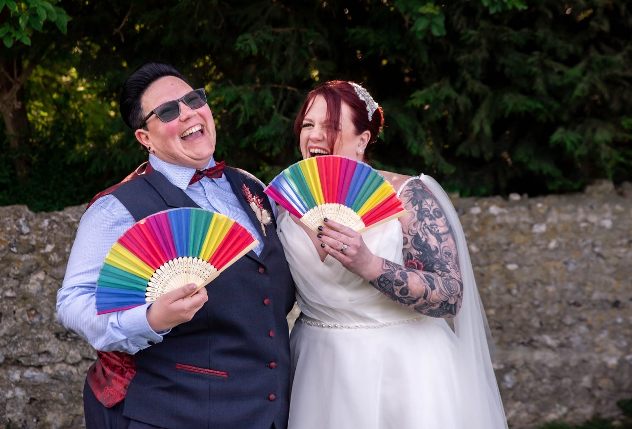 two brides holding coloured fans and laughing