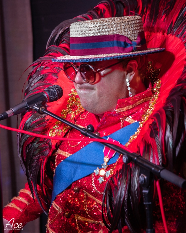 Elite Elton playing the piano in a red Elton John-inspired costume