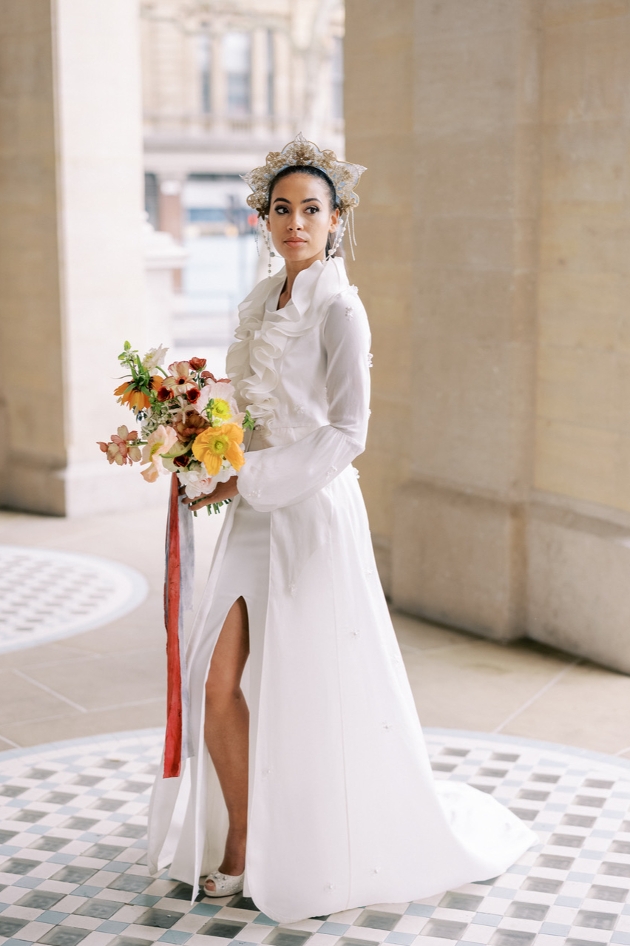 ong sleeved bridal coat worn by model holding orange and red bouquet and wearing headdress