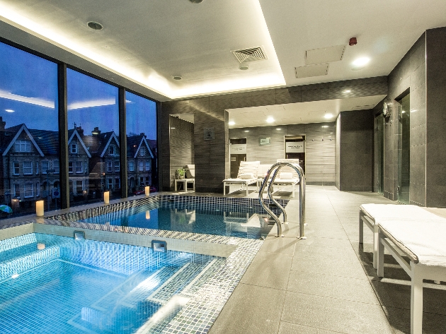 two square modern jacuzzi baths, modern grey slate walls and bed loungers around