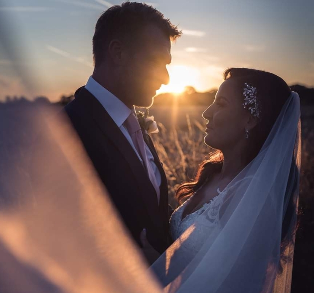 couple standing in wedding attire at sunset veil in the air