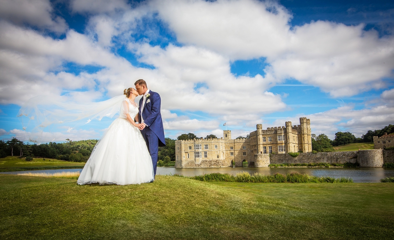 couple on grace verge by lake with castle in the background