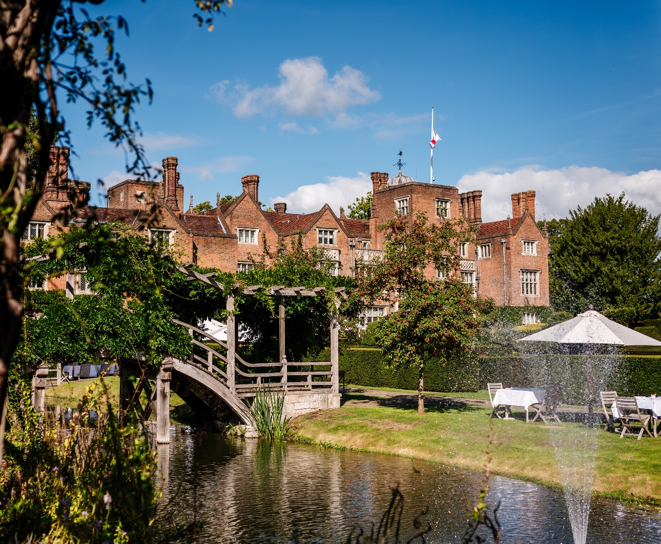 Great Fosters historic house with pond and water feature, garden chairs manicured lawns