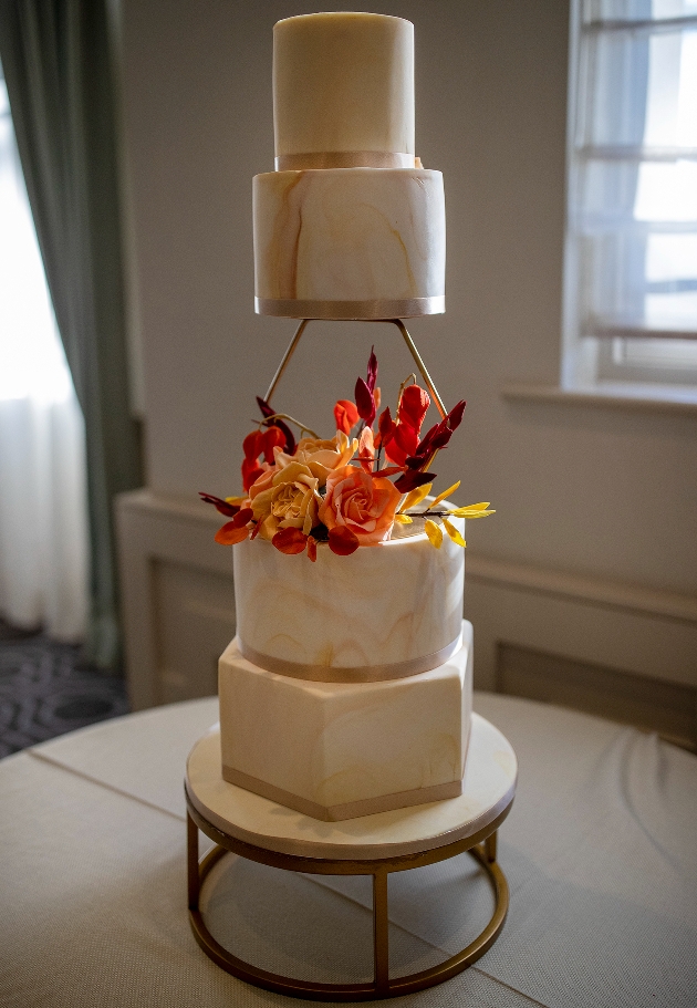 four tier cake with orange and red flowers shaped tiers and gold seperators