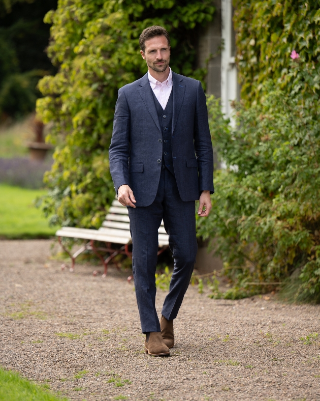 A man walking wearing a navy three-piece suit