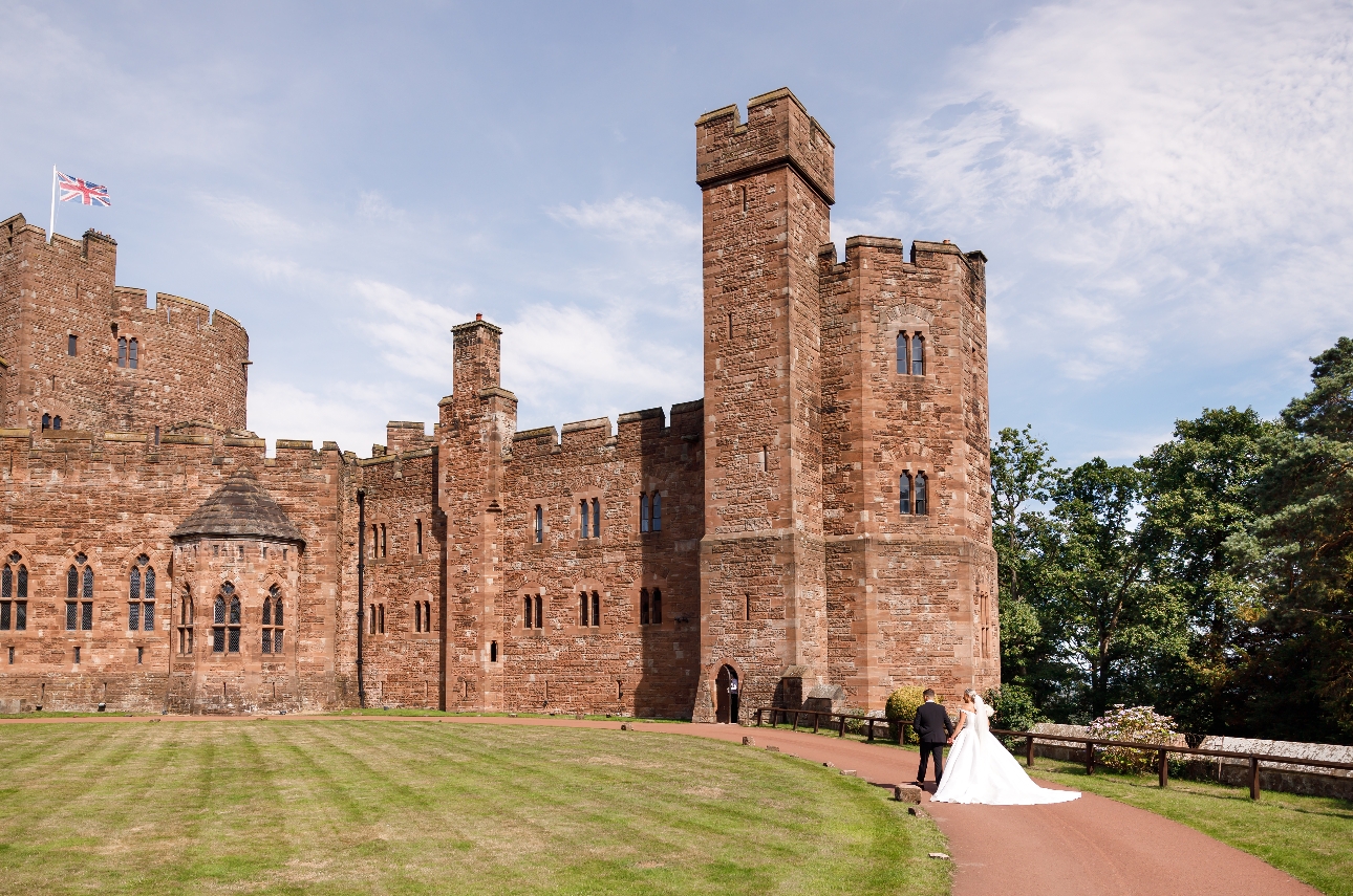 castle wedding couple walking towards it on grass