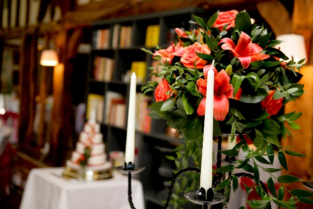 Candelabra in from of a red lily flower arrangement. Wedding cake is in teh background