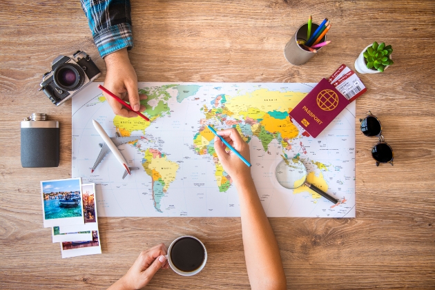 World map laid out on table with couple pointing out where to go on honeymoon. Surrounded by travel paraphenalia