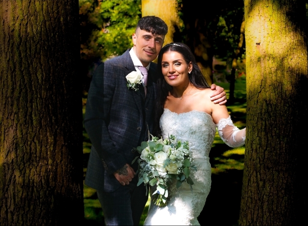 bride and groom on their wedding day standing between two trees