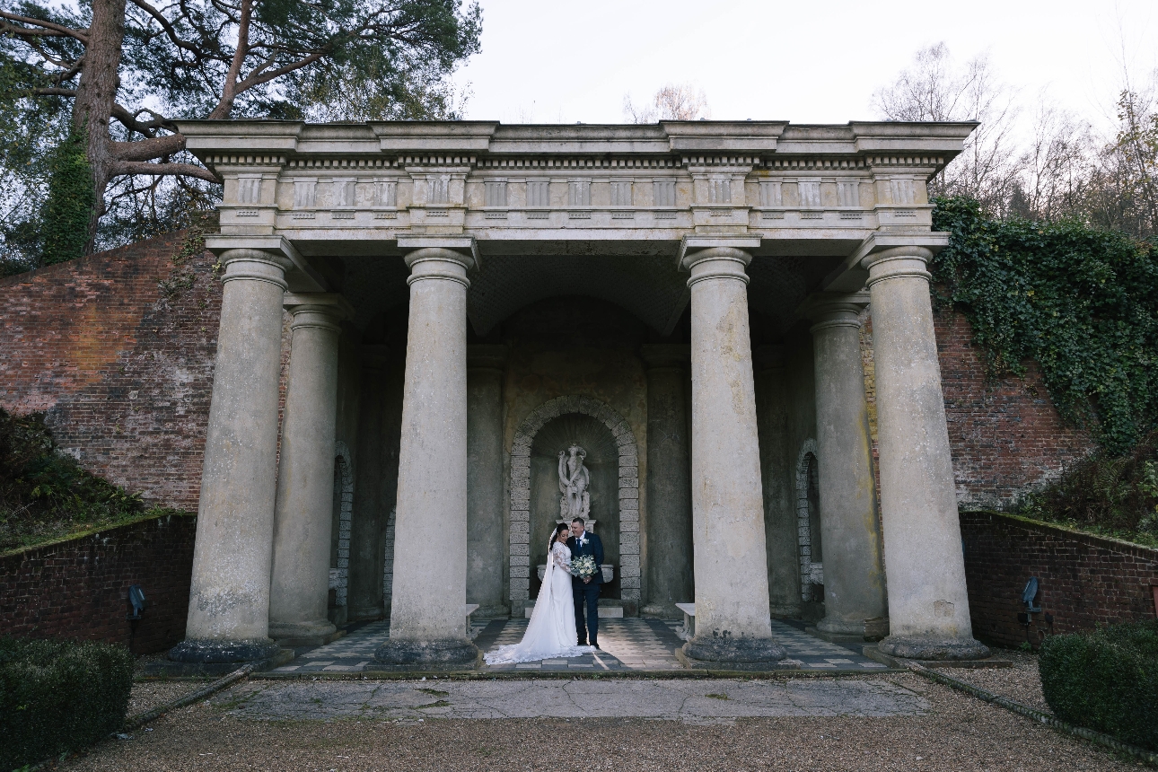 bride and groom standing outside under stone pillars