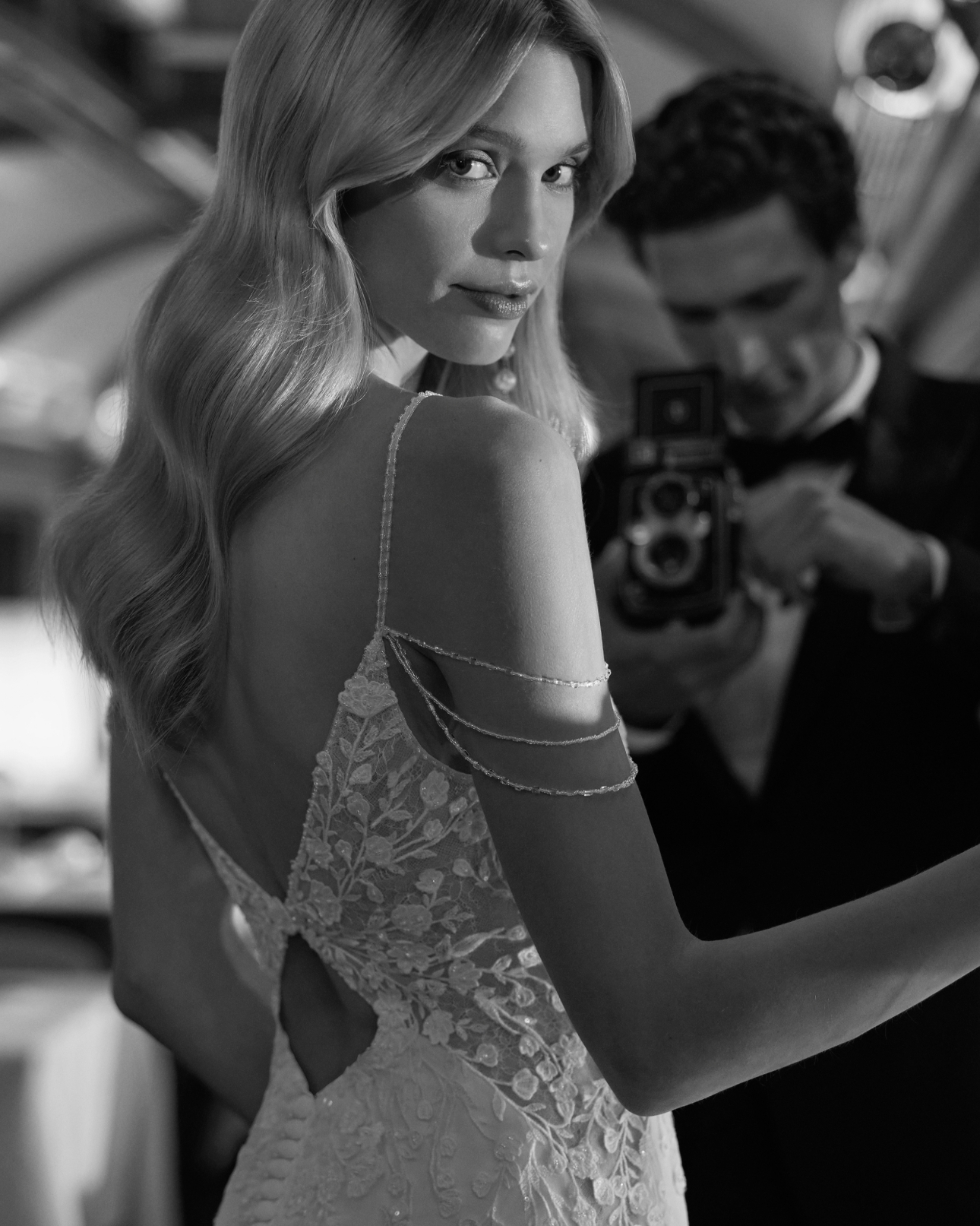 woman in strappy wedding dress posing in front of man with camera