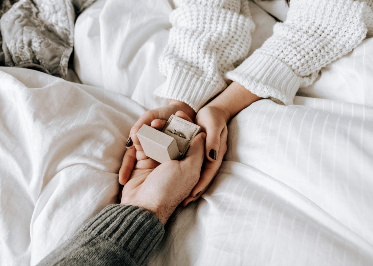 proposal in bed, hands holding a ring box